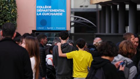 A crowd stands outside La Guicharde school.