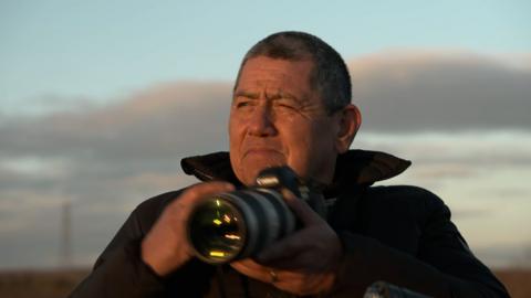 A man in the light of dusk holding a digital SLR camera