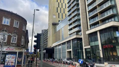 A row of cars parked in front of large buildings.