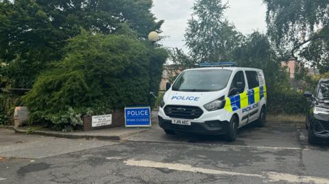 A police van and a "police road closed" sign next to a river walkway in York