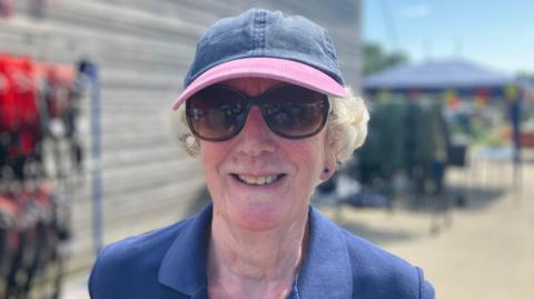 Anne, a woman, wearing a blue hat and a blue top, smiling for the camera.