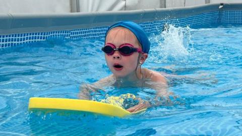 A child swimming with a float in a pop-up pool inside a marquee
