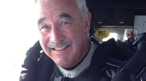 A smiling man with a grey hair and moustache in diving gear.