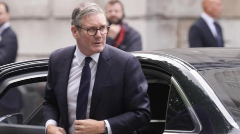 Keir Starmer look to his left as he exits a black car