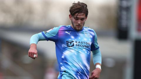 A photo of Dom Ballard, wearing a blue and purple Leyton Orient kit, playing for the O's against Northampton Town in February