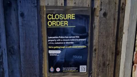 A close-up of a poster on the wooden back gate of the house that says "Closure Order, Lancashire Police has served this property with a closure notice to prevent crime, nuisance or disorder".