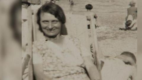 Louisa Dunne sitting in a deck chair facing the camera with other people in the background.
