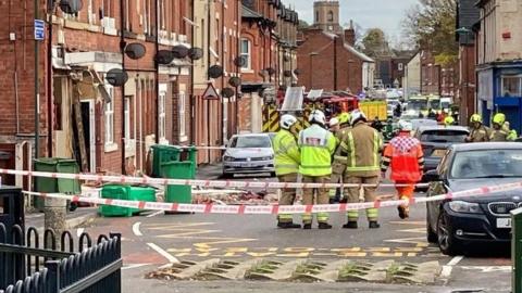 Emergency services working behind a cordon near a blown-out front of a building