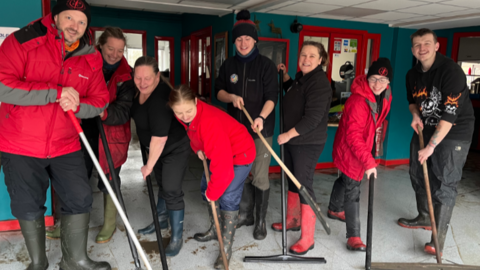 A number of people in wellies sweeping the floor of a flood-hit office