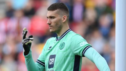 Ivo Grbic holding the post with his left hand while gesturing to his players with his right in a match for Sheff Utd