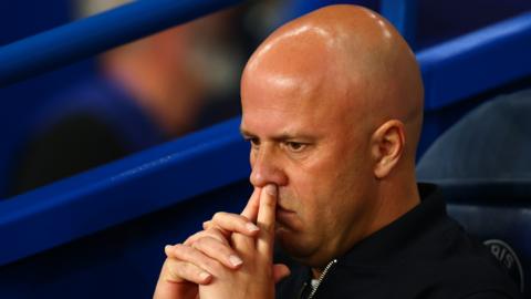 Headshot of Arne Slot, sitting on the bench, fingers on top lip, looking pensive