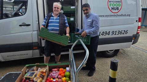 Two men are unloading green food baskets from a van.