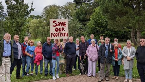 group of people standing with a save out footpath sign