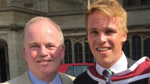 A head and shoulders image of Nick Apperley and his son Harry. They are both smiling and looking into the camera. Nick has a cream coloured jacket over a light blue shirt. Harry has a dark coloured jacket over a white shirt and a navy and green tie. 