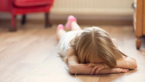 A child covers her face whilst having a tantrum on the floor.