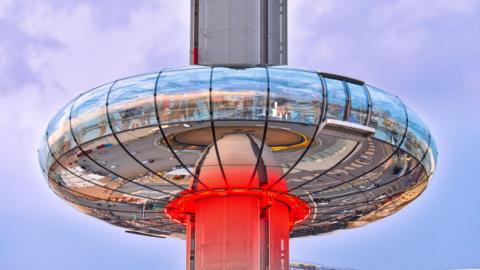 The Brighton i360 viewing pod, halfway up and lit up with a red light.