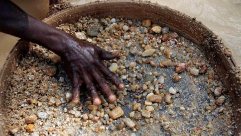 The hand of a diamond miner in Sierra Leone has he sieves gravel and smaller stones in the hope of finding the precious gems