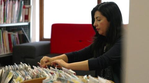 A woman looks through books on a library shelf