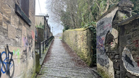 A cobbled alleyway going uphill with graffiti sprayed across the walls on each side.  