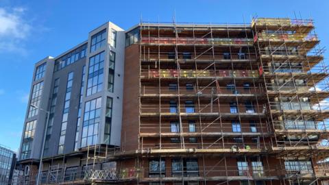 A seven-storey building, which is partially completed, is surrounded by scaffolding.