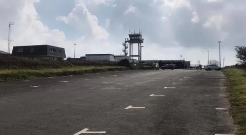 An empty car park with a airport tower in the background. 