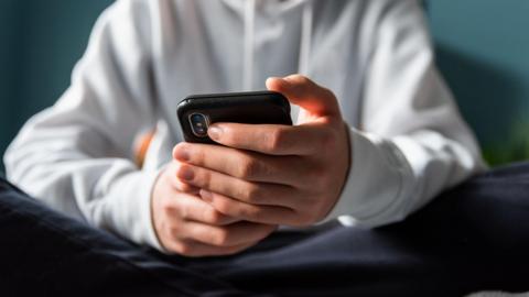 Close up of hands of teen boy in a white hoodie texting on phone.