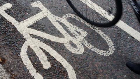 An image of a bicycle is drawn on the tarmac in white paint to denote a cycle path. On the right is the lower part of a bicycle wheel.
