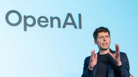 Open AI CEO Sam Altman speaks during a talk session with SoftBank Group CEO Masayoshi Son at an event titled "Transforming Business through AI" in Tokyo, Japan - he has his hand held up and appears to be mid saying something, with the OpenAI logo on the wall behind him