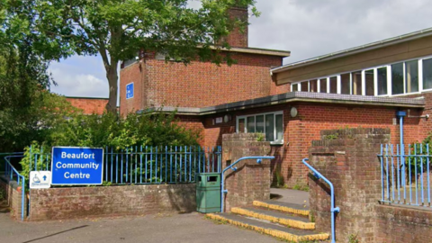 Beaufort Community Centre is a large red brick building with multiple floors extended over three main structures. Outside is a large blue sign saying Beaufort Community Centre.