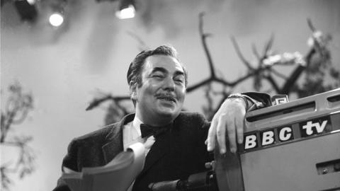 Sydney Newman holding a script leaning on a BBC TV camera