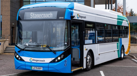 A close up of a blue and white Stagecoach bus parked in front of a modern building