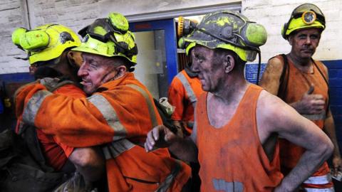 Men blackened by working in a mine shaft embrace each other on the final day of production at Kellingley Colliery.