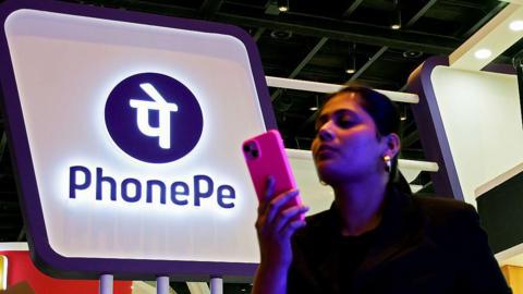 A woman checks her mobile phone close to 'PhonePe' logo installation on the last day of the sixth Global Fintech Fest (GFF) in Mumbai. The three day event held from 7-9th October 2025, a global platform to encourage major stakeholders of Fintech firms, who gathered to share and exchange ideas, and innovation in banking, finance, artificial intelligence, digital payments, startups, and new technologies concluded on the last day with Indian Prime Minister Narendra Modi and United Kingdom Prime Minister, Keir Starmer addressing the delegates present at the event. (Photo by Ashish Vaishnav/SOPA Images/LightRocket via Getty Images)