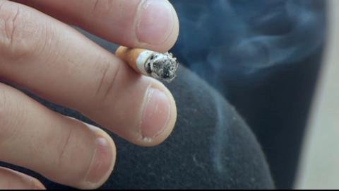 A man's hand holding a cigarette smoked almost to the bottom