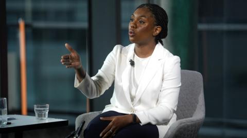 Kemi Badenoch wearing a white jacket and t-shirt
