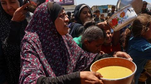 Palestinians line up to receive a hot meal at a food distribution point in the Al-Rimal neighbourhood in Gaza City in the central Gaza Strip on May 21, 2025