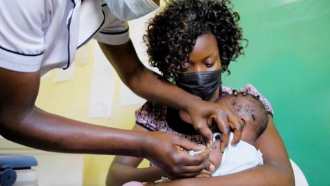 A mother cradles a baby as he receives a jab in the arm