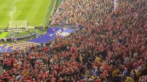 A crowd at Boston Stadium, with many thousands of Scotland fans in blue football strips and orange football strips. 