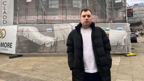 James Greenwood in front of a building undergoing cladding remediation