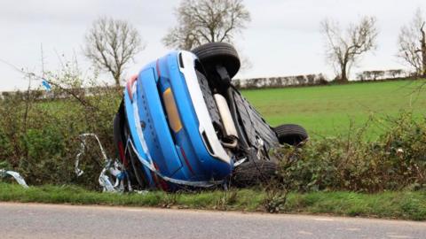 A blue Vauxhall car upside down in a ditch