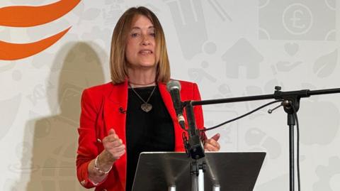 Jane Dodds in a red jacket on the microphone