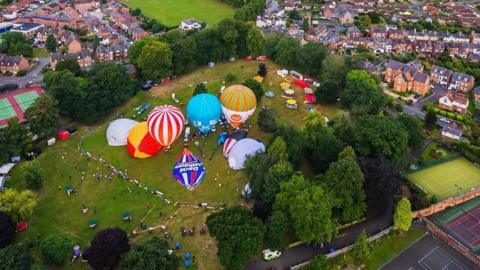 Lots of hot air balloons in the centre of a park