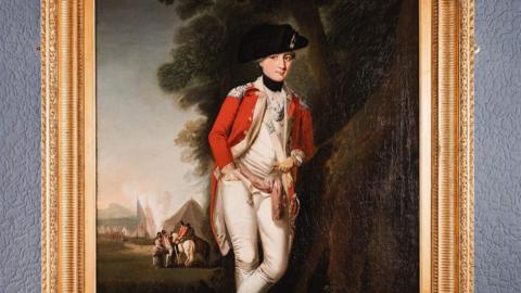 An oil painting of Paul Crebbin. He is wearing a red greatcoat and white uniform underneath, with a black hat on his head. There is a tent in the background and two people on a horse speaking to others on foot.