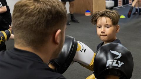 A boy practices boxing while wearing gloves