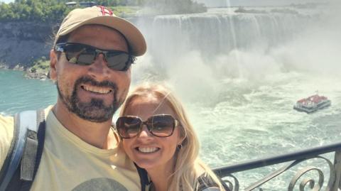 Man and woman wearing sunglasses smiling in front of a waterfall 