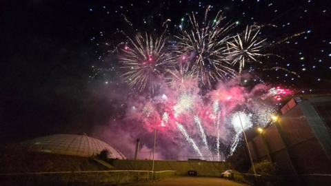 Pink and purple fireworks light up a night sky above a white domed building