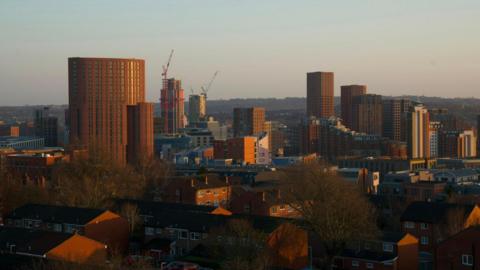 A skyline picture of Leeds city centre. The picture is taken at dawn, with the sun illuminating apartment buildings.