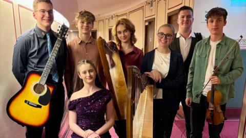 Seven members of Scran stand in a group holding their musical instruments. They are aged between 13 and 17.
