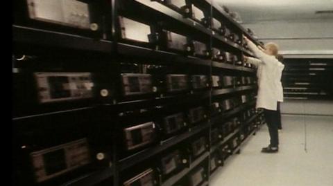 A man in a white coat in a room full of video machines.