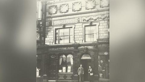 An undated black and white image of the exterior of the Angel Inn in Stockport with a man and a woman standing at the entrance.